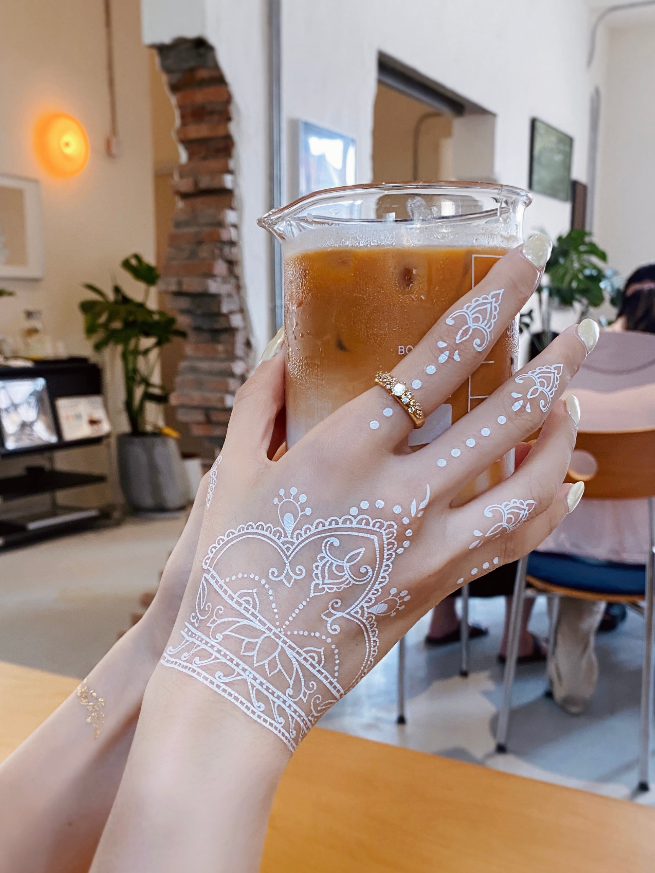 Hand with white henna design holding a coffee cup in a casual setting