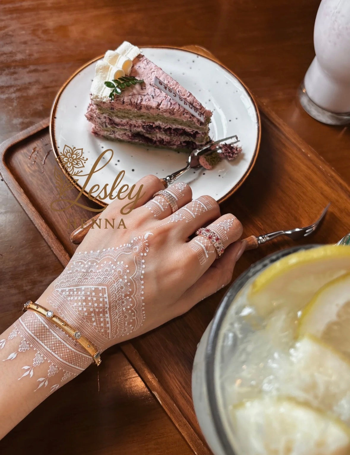 Hand with intricate henna designs holding a fork over a slice of cake on a wooden table.